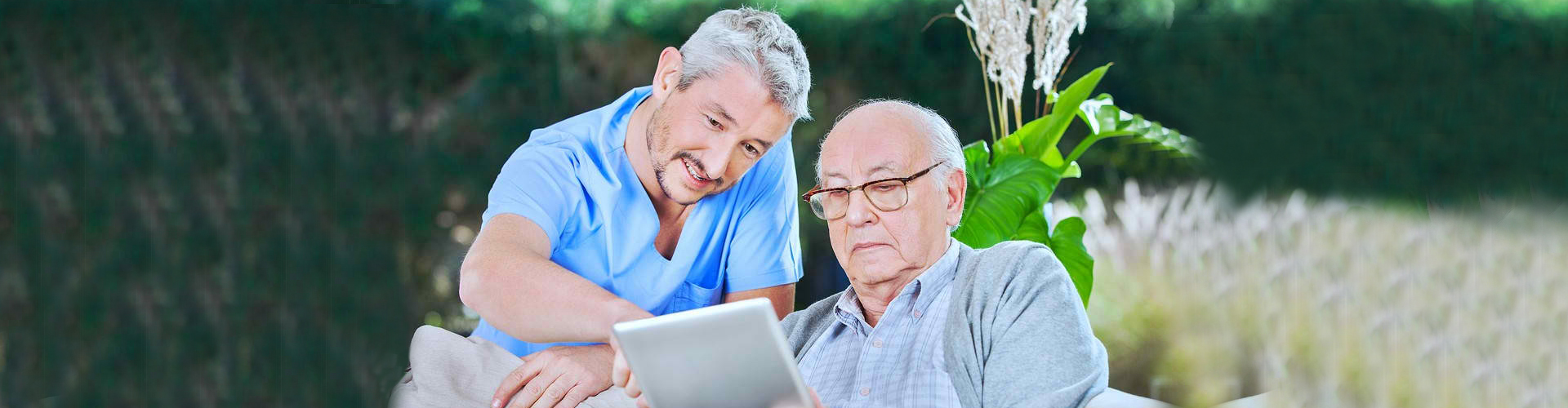 caregiver assisting elder man on using a tablet